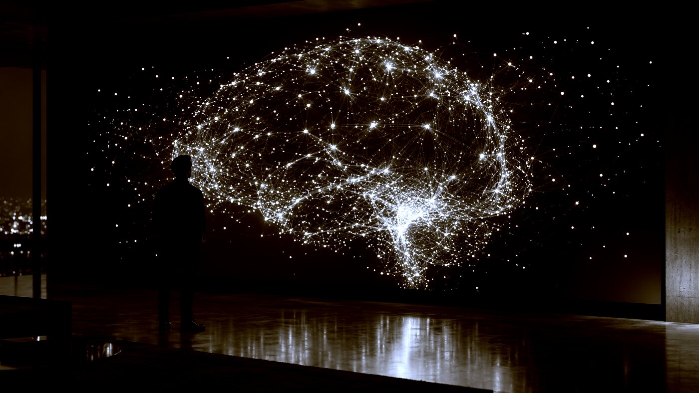 A person in front of a wall screen showing a glowing network shaped like a brain